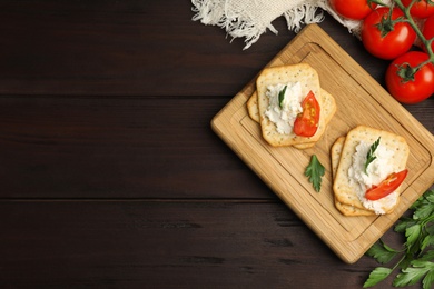 Delicious crackers with cream cheese, tomato and parsley on wooden table, flat lay. Space for text