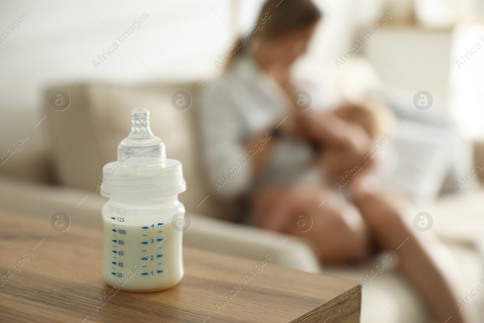 Photo of Mother breastfeeding her little baby at home, focus on bottle with milk. Healthy growth