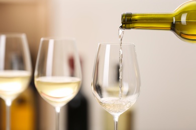 Photo of Pouring wine from bottle into glass on blurred background, space for text