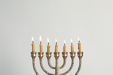 Photo of Golden menorah with burning candles on light grey background, space for text