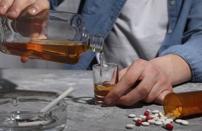 Photo of Alcohol and drug addiction. Man pouring whiskey into glass at grey textured table, closeup