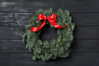 Photo of Christmas wreath made of fir tree branches with red ribbon on black wooden background