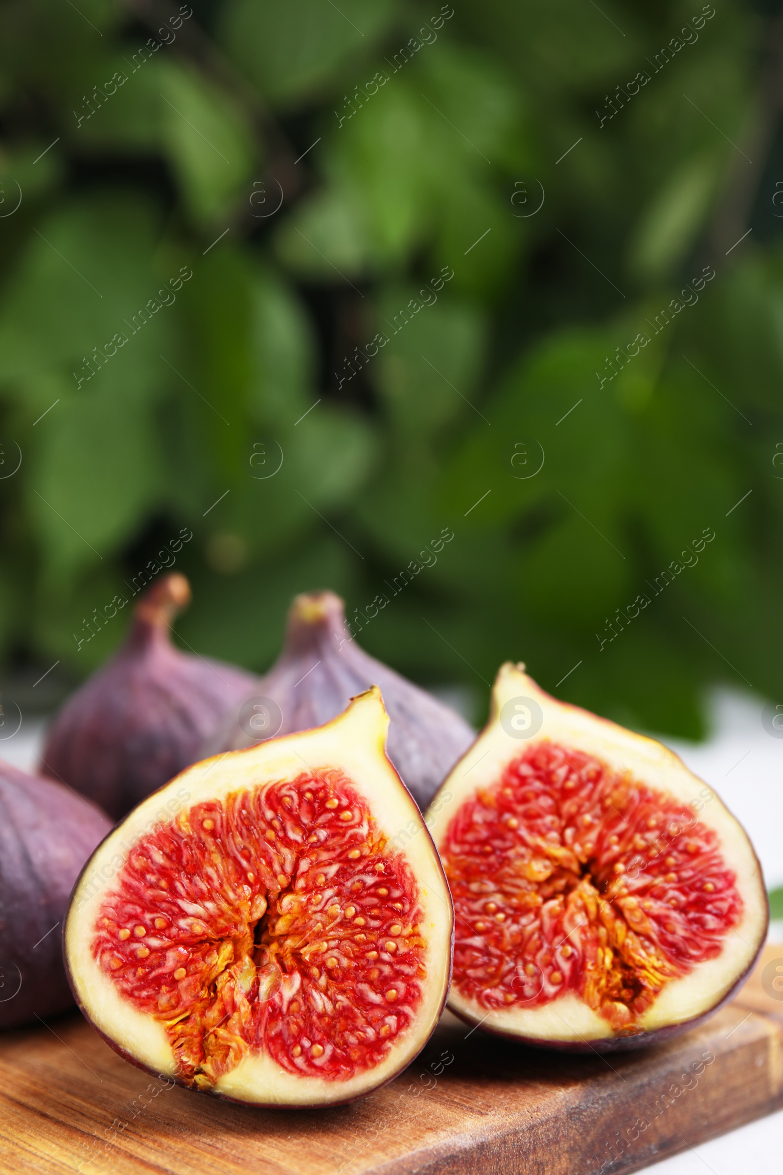 Photo of Tasty ripe figs on wooden board against blurred background