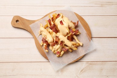 Photo of Delicious French fries with bacon and cheese sauce on wooden table, top view