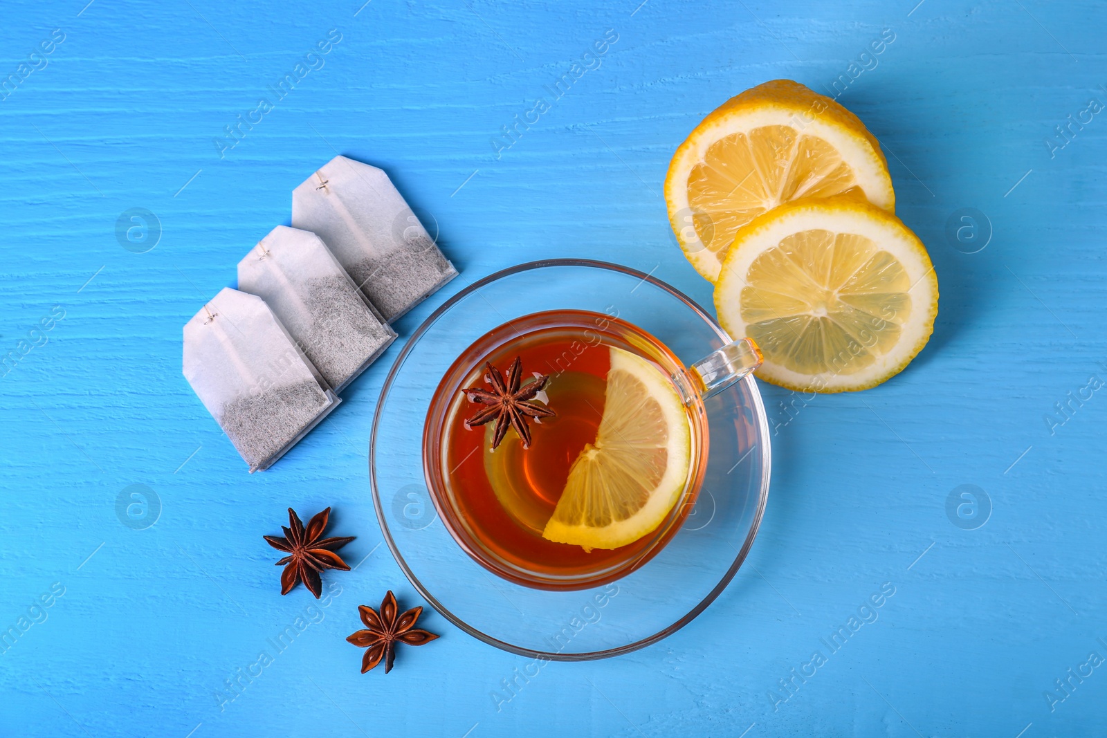 Photo of Tea bags, cup of hot drink, anise stars and lemon on light blue wooden table, flat lay
