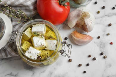 Flat lay composition with pickled feta cheese in jar on white marble table