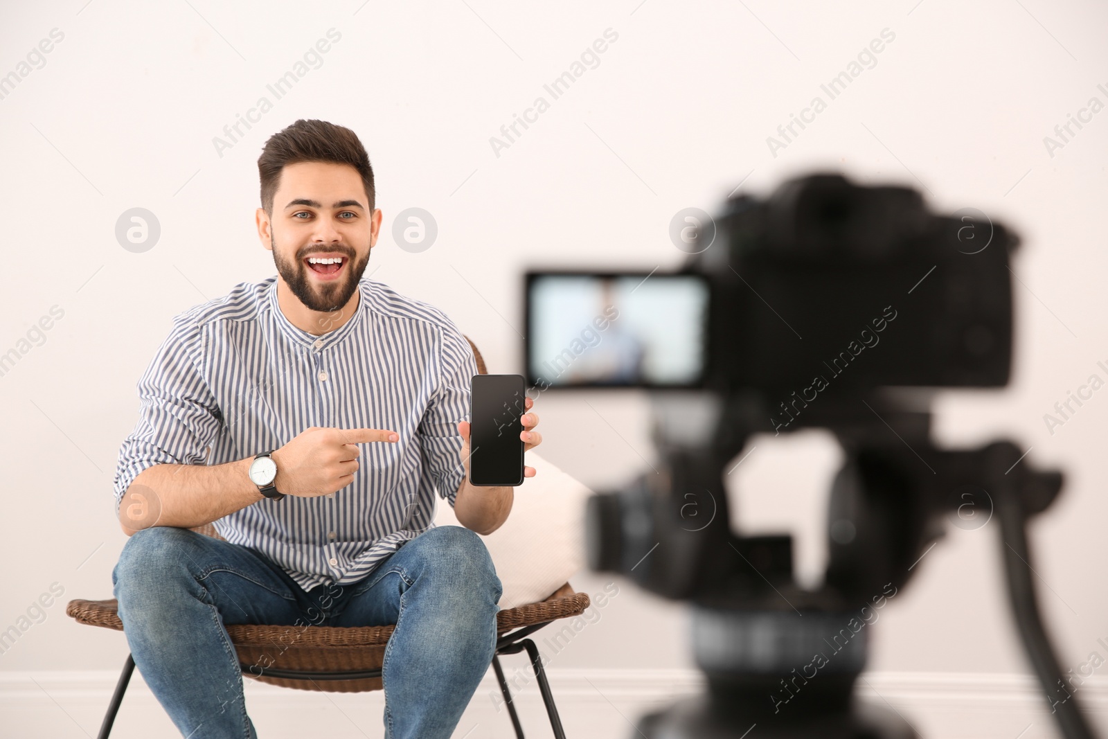 Photo of Young blogger with smartphone recording video on camera indoors