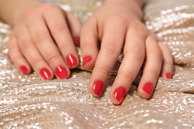 Photo of Woman with red manicure on gold fabric, closeup. Nail polish trends