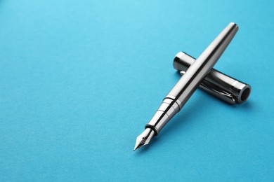 Stylish silver fountain pen with cap on light blue background, closeup. Space for text