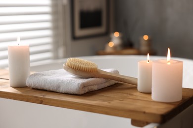 Photo of Wooden tray with burning candles, towel and brush on bathtub in bathroom