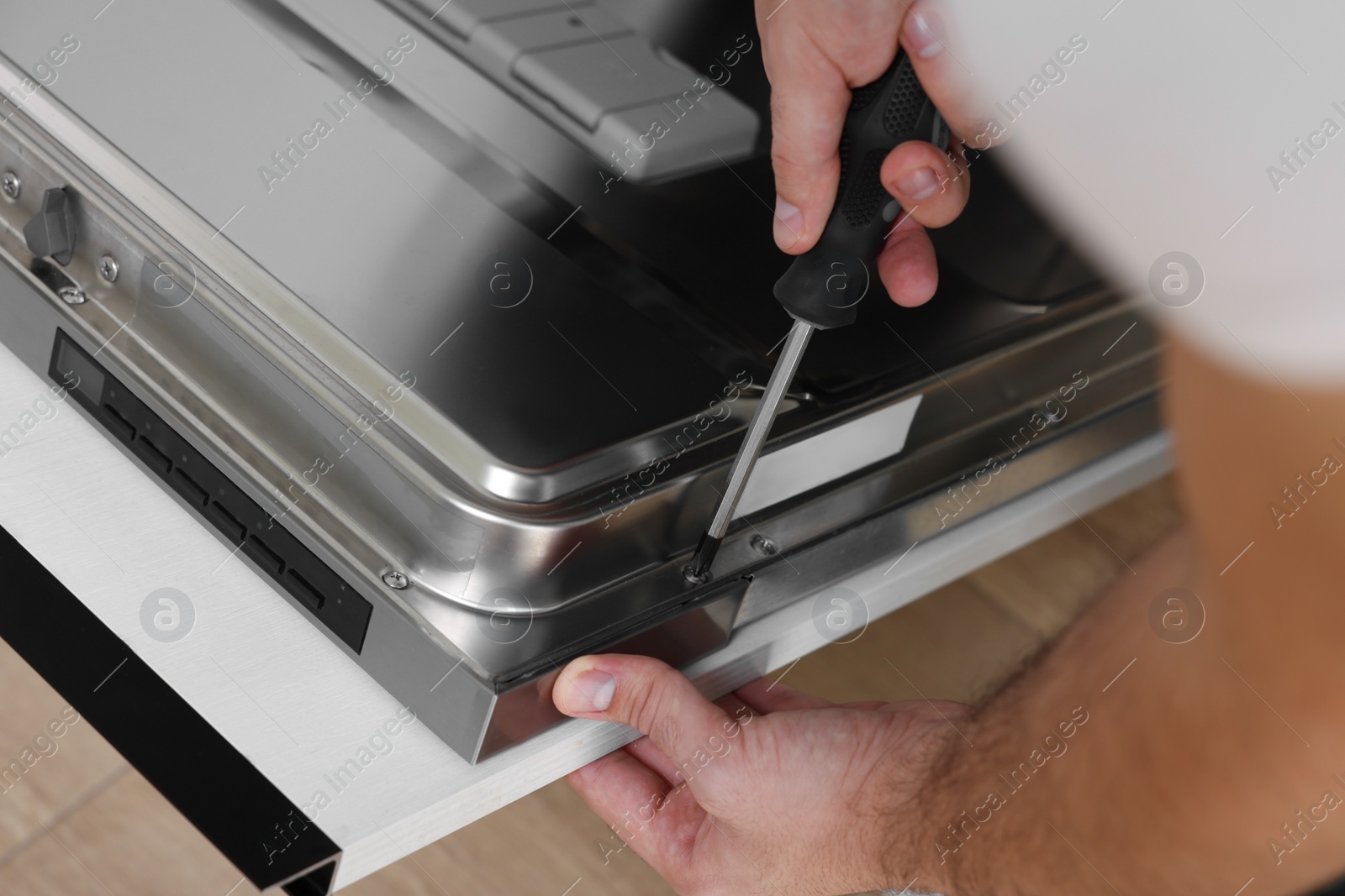 Photo of Serviceman repairing dishwasher door with screwdriver indoors, closeup