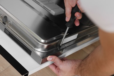 Photo of Serviceman repairing dishwasher door with screwdriver indoors, closeup