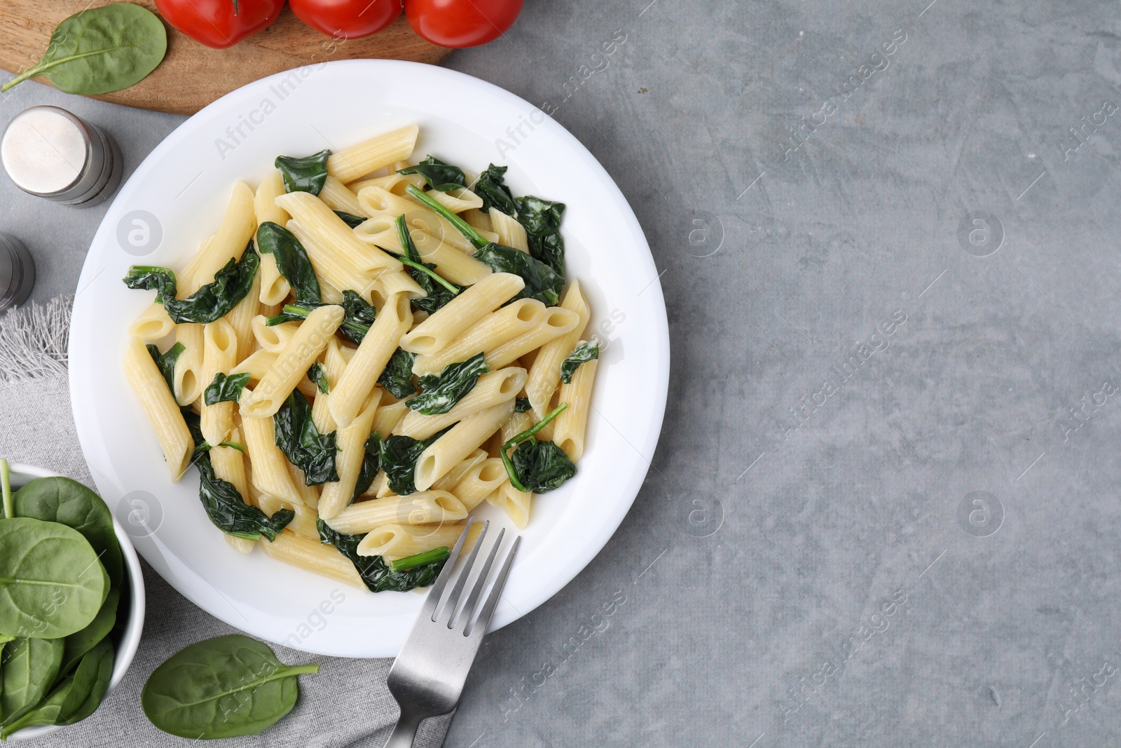 Photo of Tasty pasta with spinach and sauce served on grey textured table, flat lay. Space for text