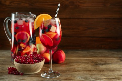 Photo of Glass and jug of Red Sangria with fruits on wooden table. Space for text