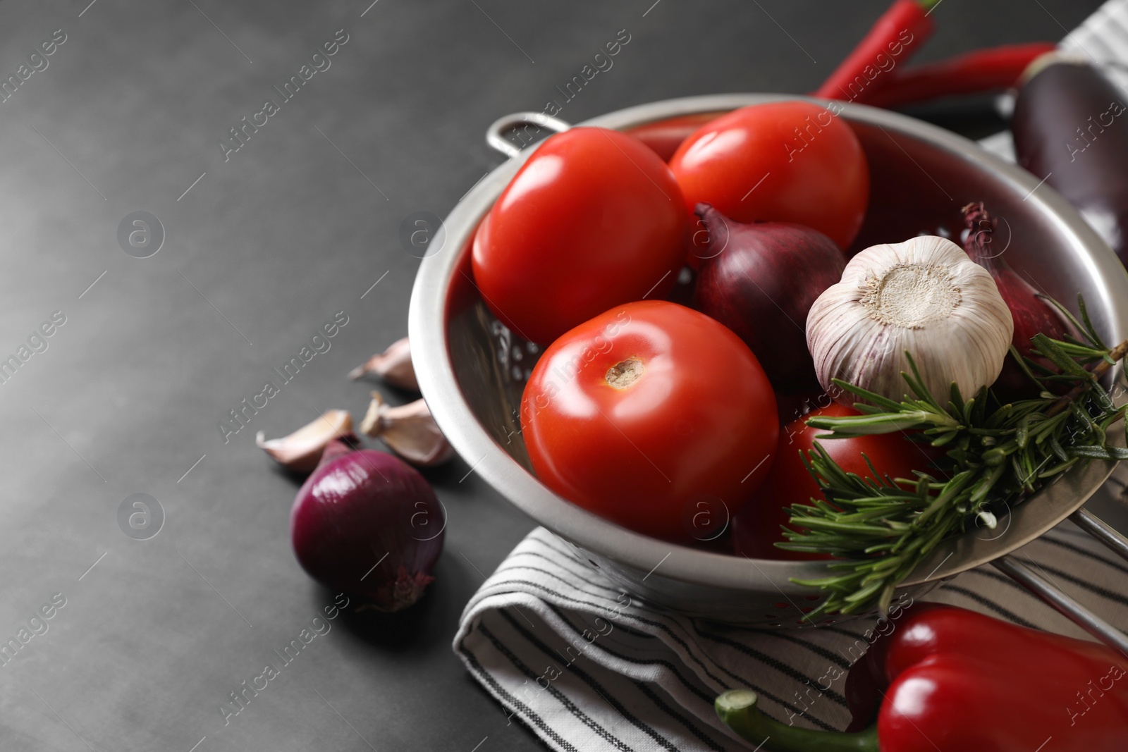 Photo of Cooking delicious ratatouille. Fresh ripe vegetables and colander on dark grey table, closeup. Space for text