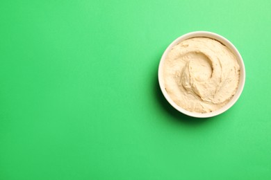 Bowl of tasty hummus on green background, top view. Space for text