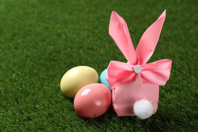 Easter bunny gift bag and dyed eggs on green grass, space for text