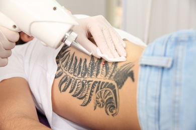 Photo of Young woman undergoing laser tattoo removal procedure in salon, closeup