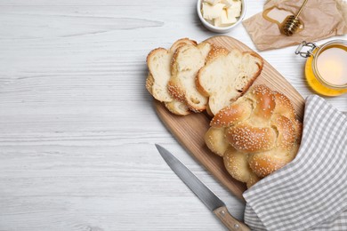 Photo of Cut freshly baked braided bread, honey and butter on white wooden table, flat lay with space for text. Traditional Shabbat challah