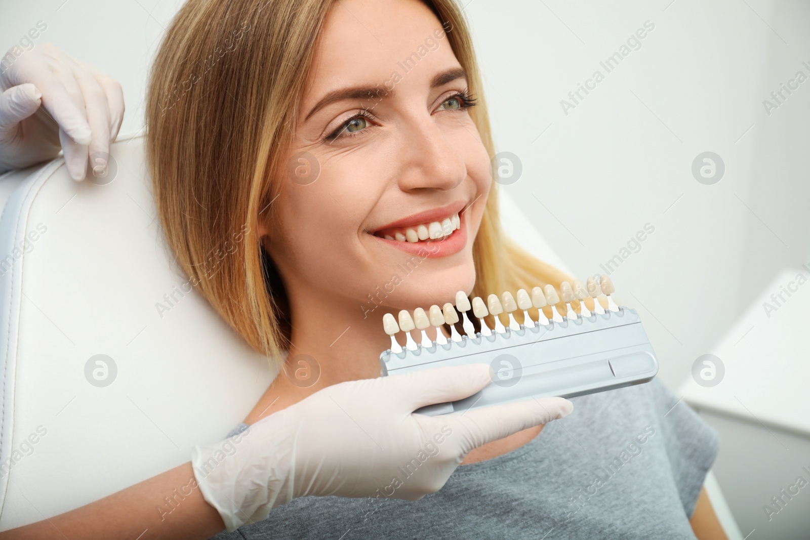 Photo of Doctor matching patient's teeth color with palette in clinic, closeup. Cosmetic dentistry