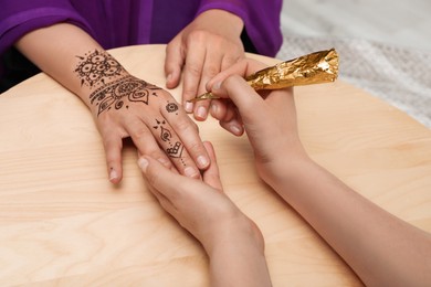 Photo of Master making henna tattoo on hand at wooden table, closeup. Traditional mehndi