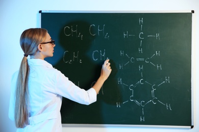 Female scientist writing chemical formula on chalkboard indoors