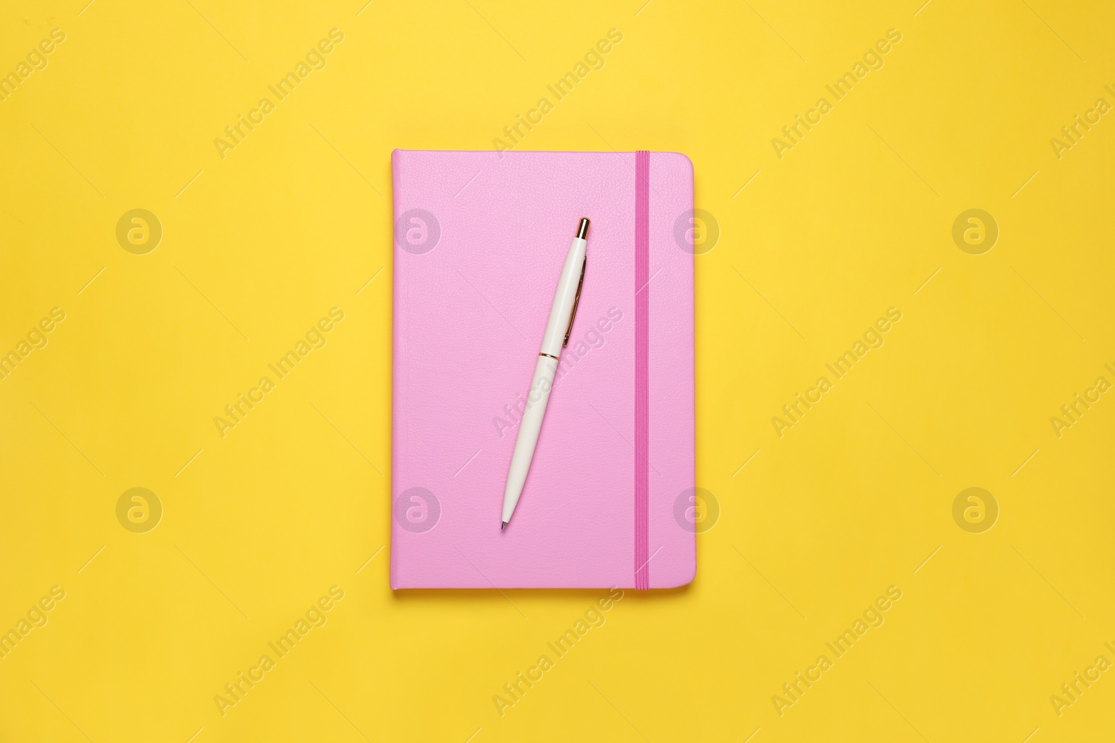 Photo of Closed pink notebook and pen on yellow background, top view