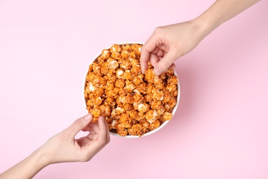 Women eating tasty popcorn from paper bucket on color background, top view