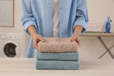 Photo of Woman with folded clean terry towels at table in laundry room, closeup