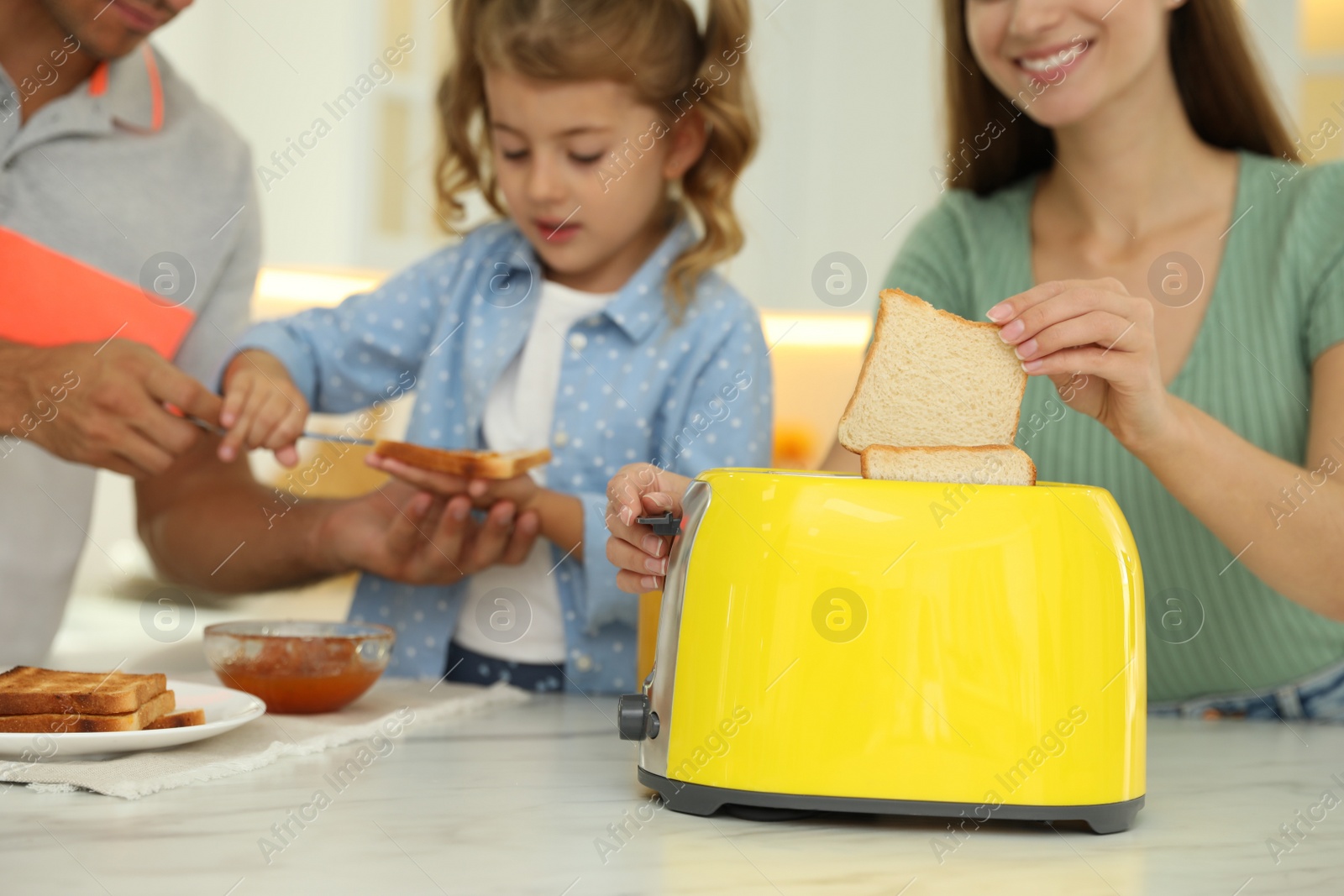 Photo of Happy family having breakfast with toasted bread at table in kitchen, closeup