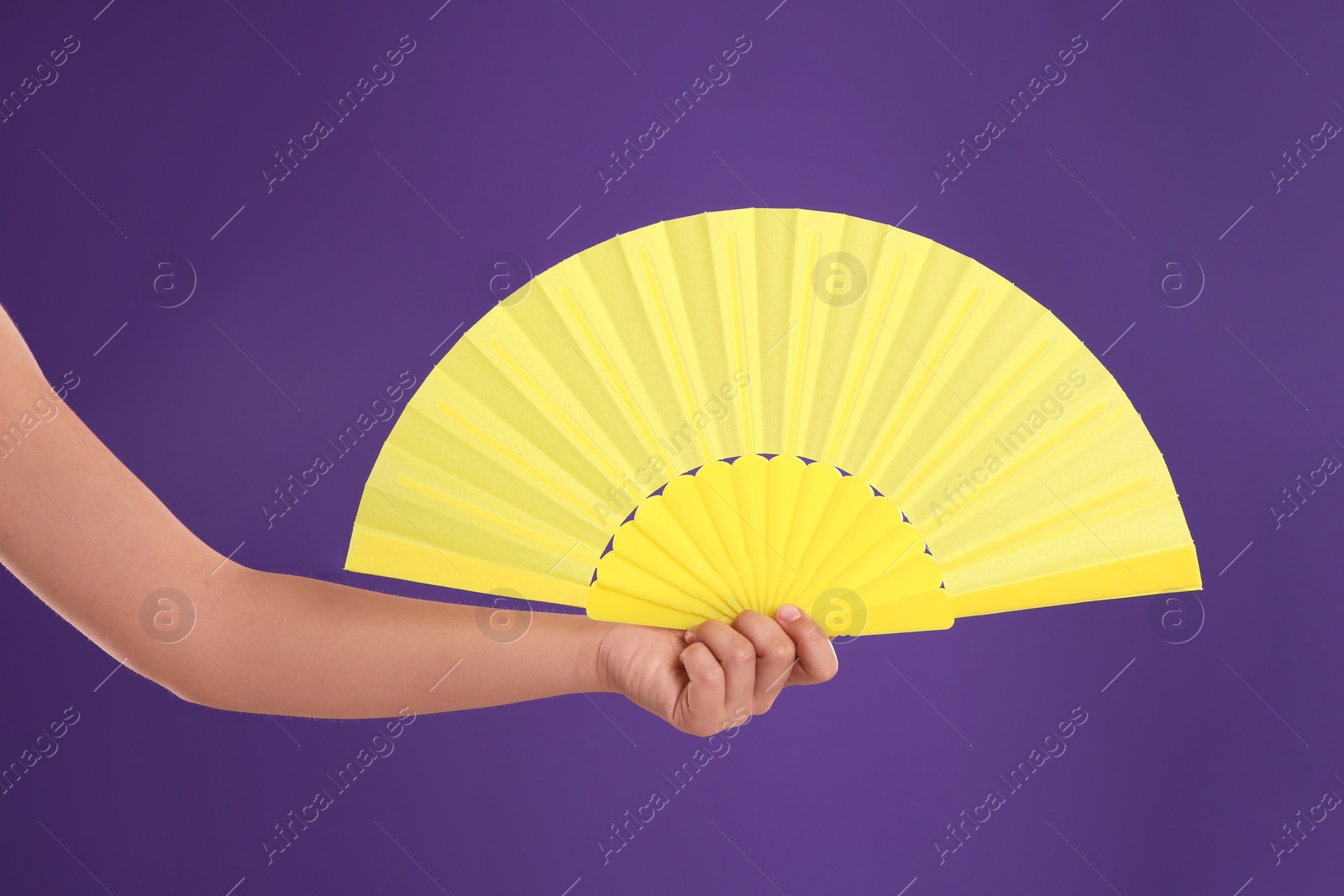 Photo of Woman holding yellow hand fan on purple background, closeup