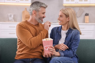 Photo of Happy affectionate couple with popcorn spending time together on sofa at home. Romantic date