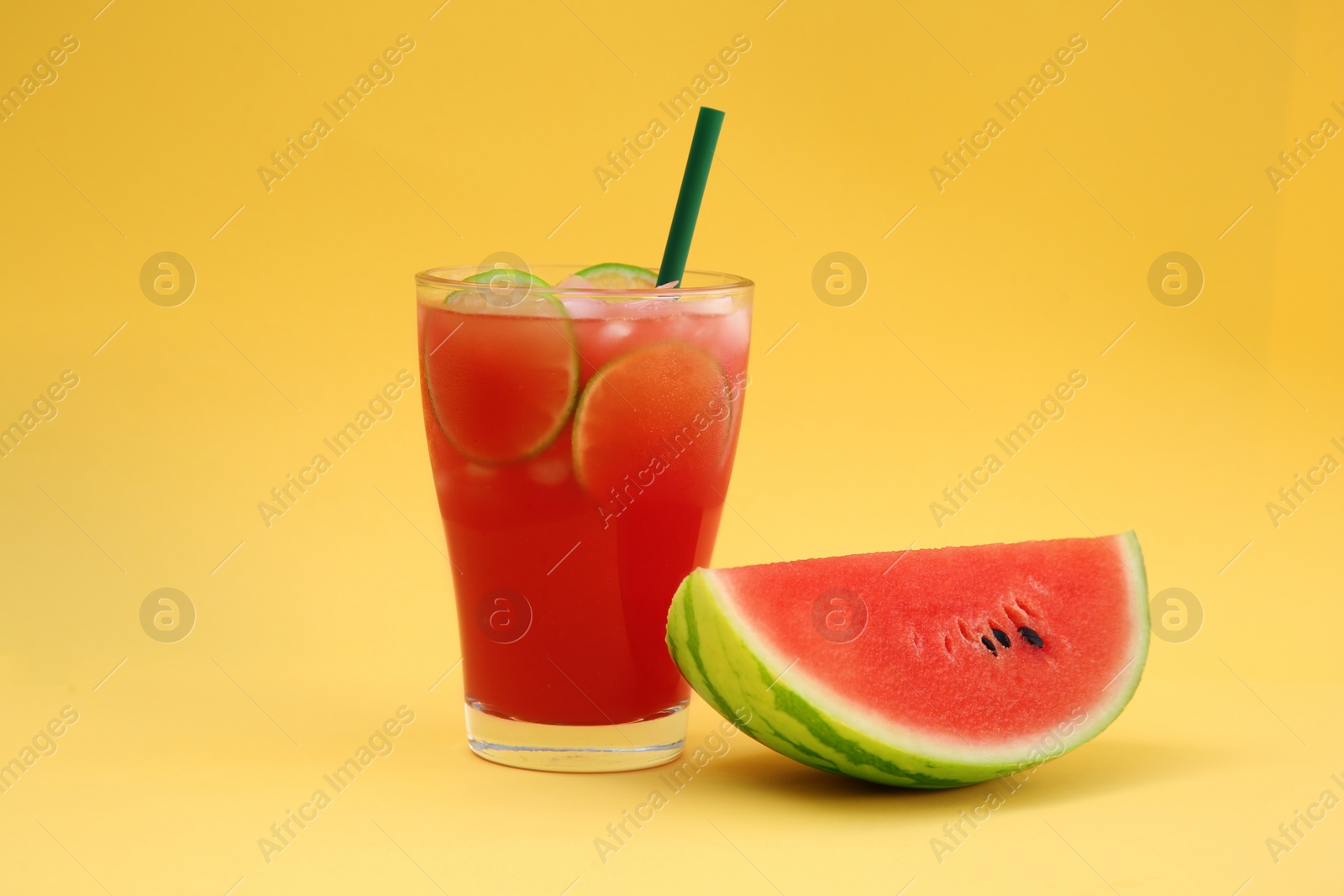 Photo of Glass of delicious drink with lime slices, ice cubes and fresh watermelon on yellow background