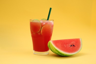 Glass of delicious drink with lime slices, ice cubes and fresh watermelon on yellow background