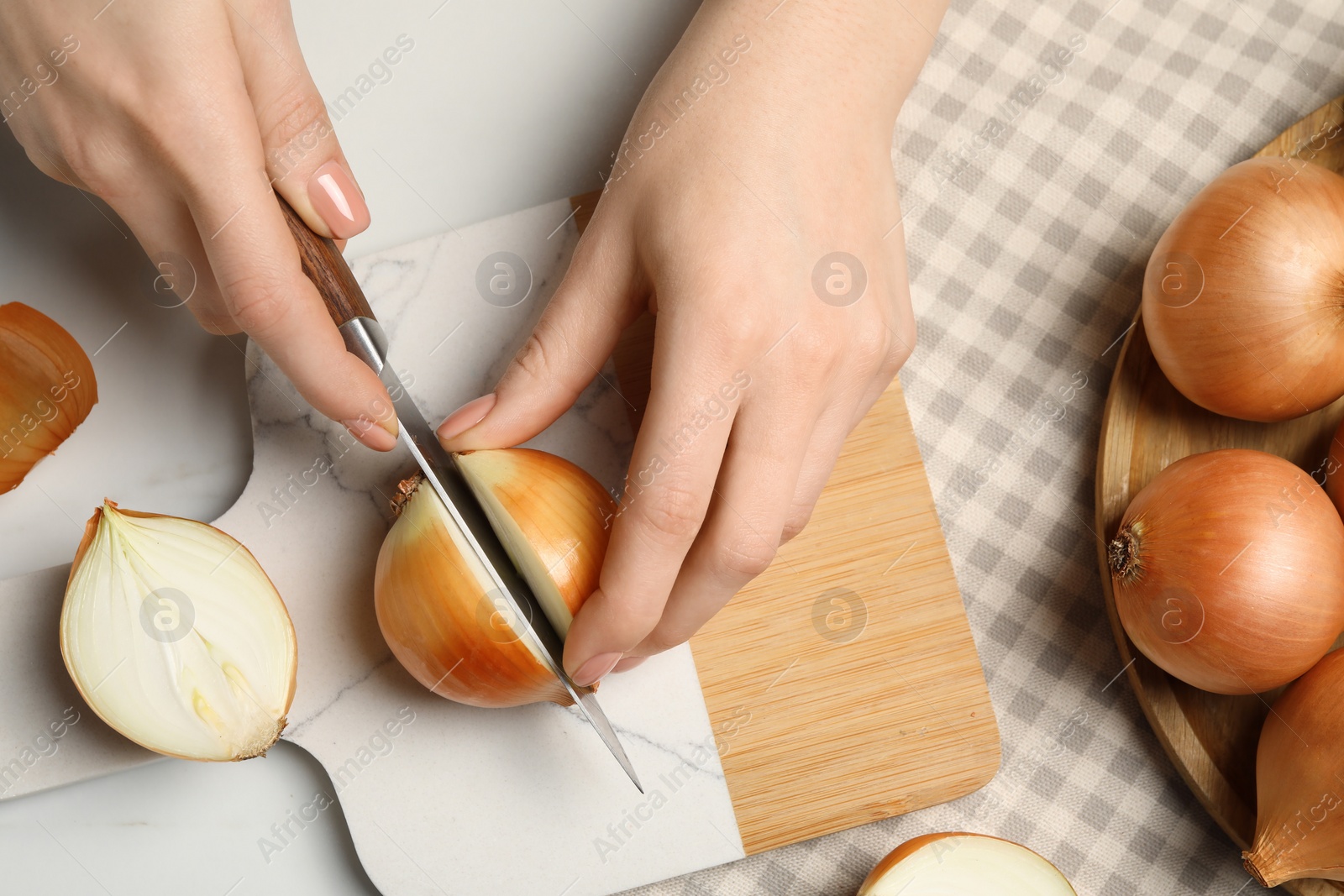 Photo of Woman cutting ripe onion at white marble table, top view