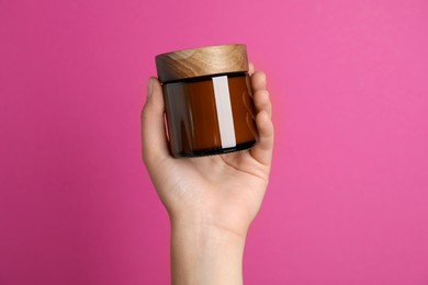 Photo of Woman holding jar of face cream on pink background, closeup