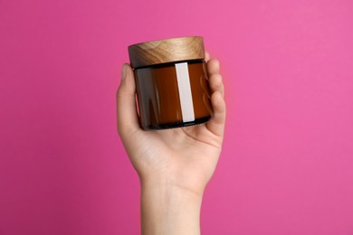 Woman holding jar of face cream on pink background, closeup