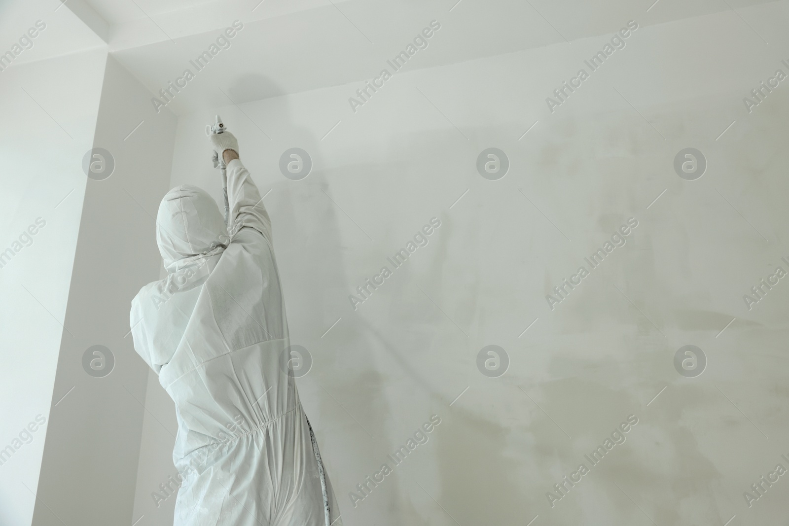 Photo of Decorator painting wall with spray, back view. Space for text