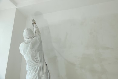 Photo of Decorator painting wall with spray, back view. Space for text