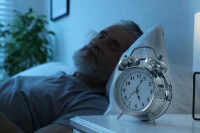 Photo of Senior man sleeping in bed at home, focus on alarm clock. Space for text