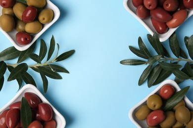 Different fresh olives and green leaves on light blue background, flat lay. Space for text