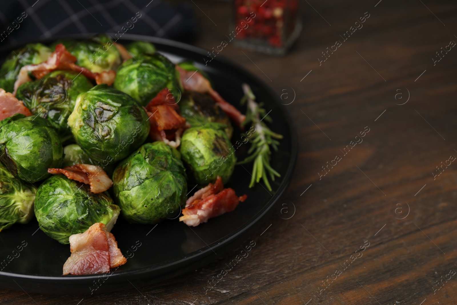 Photo of Delicious roasted Brussels sprouts and bacon on wooden table, closeup. Space for text