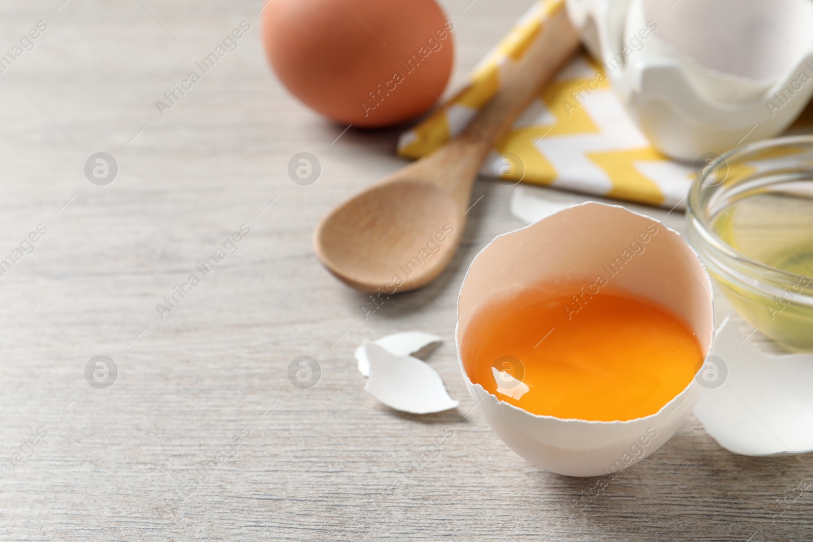 Photo of Cracked eggshell with raw yolk on white wooden table, space for text