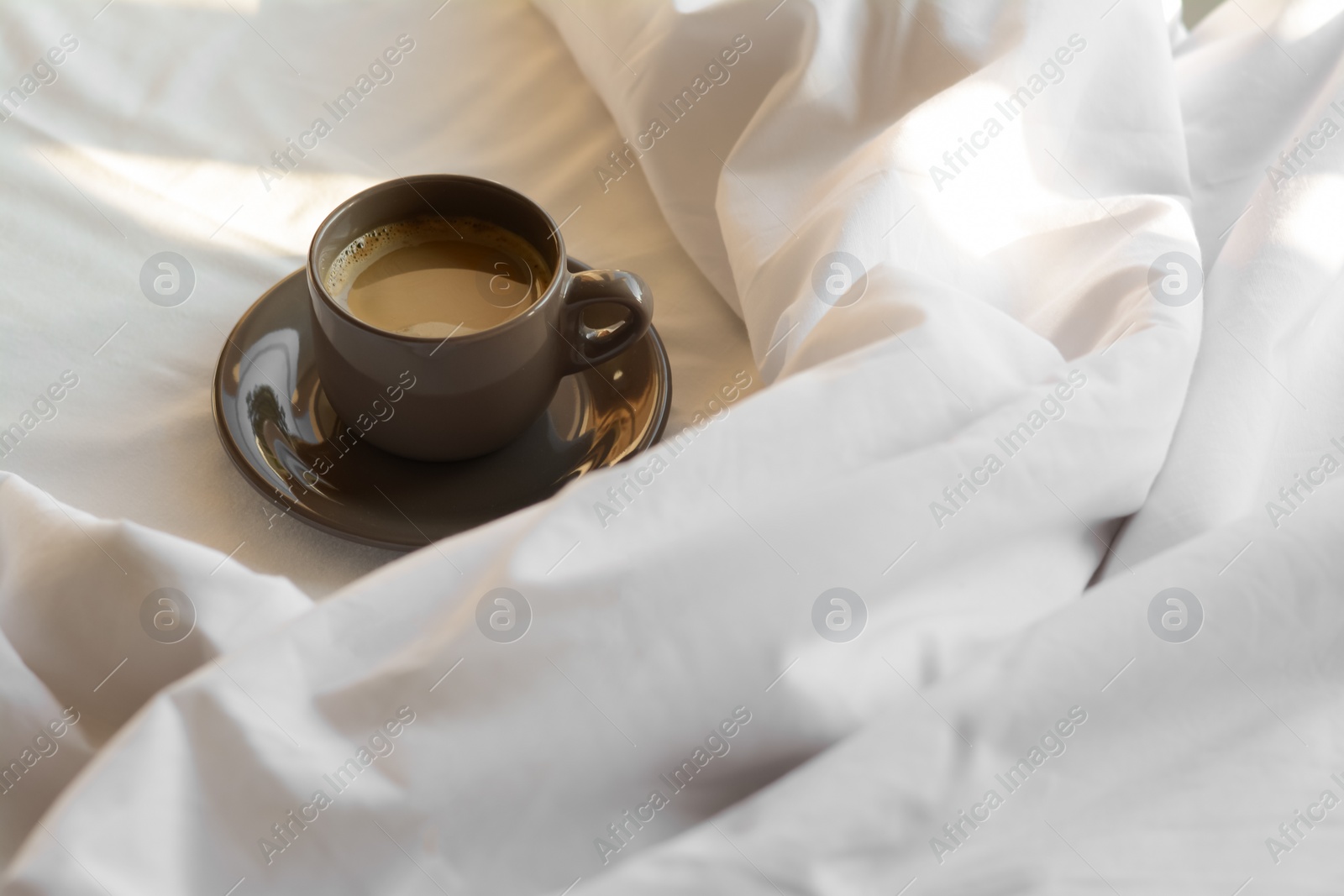 Photo of Cup of aromatic morning coffee on bed