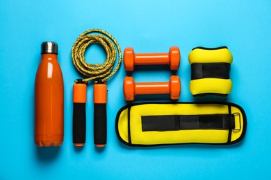 Photo of Yellow weighting agents and sport equipment on light blue background, flat lay