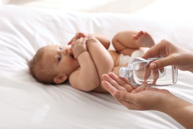 Mother with bottle of massage oil near baby on bed, closeup