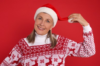 Happy senior woman in Christmas sweater and Santa hat on red background