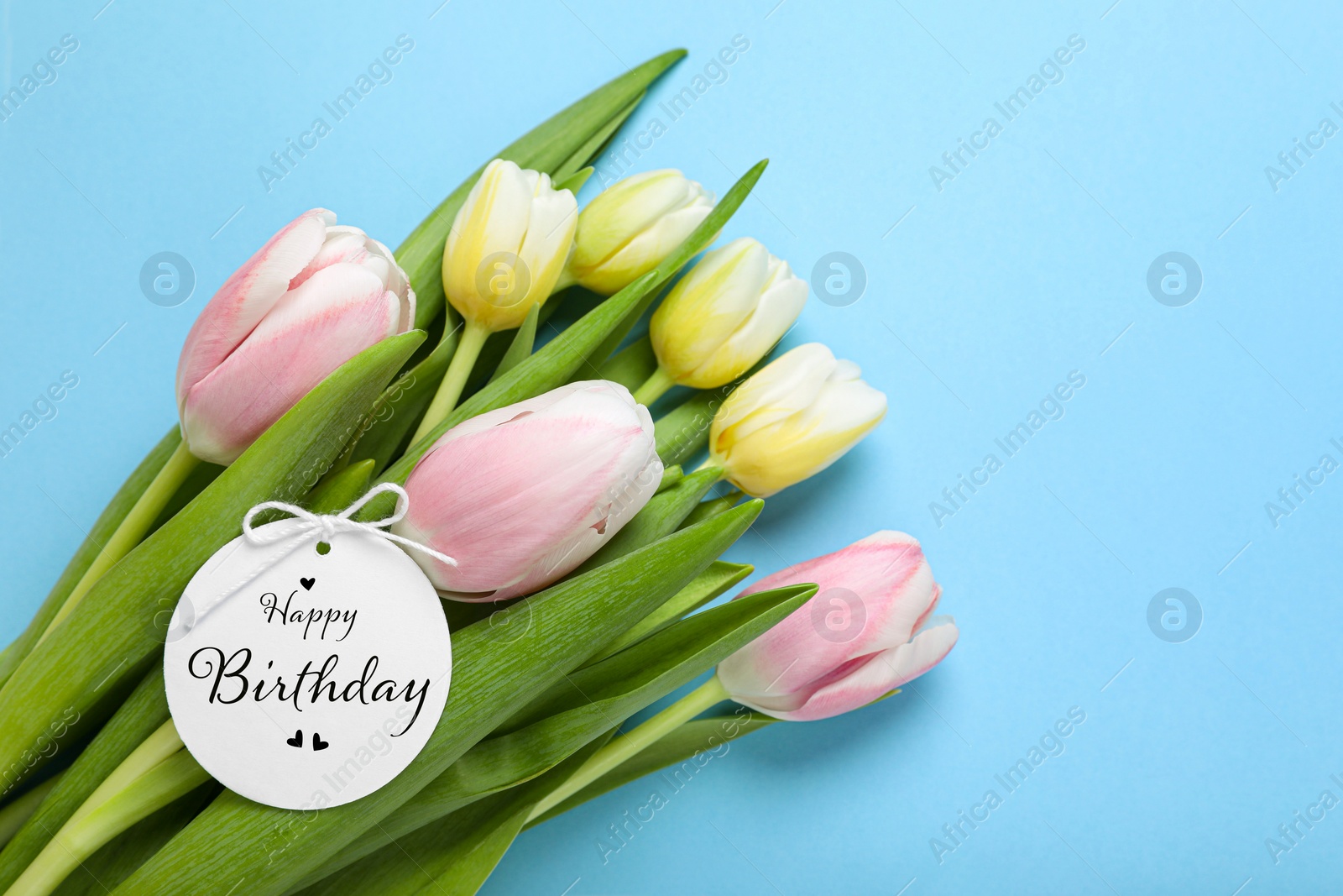 Image of Beautiful bouquet of tulip flowers with Happy Birthday card on light blue background, space for text