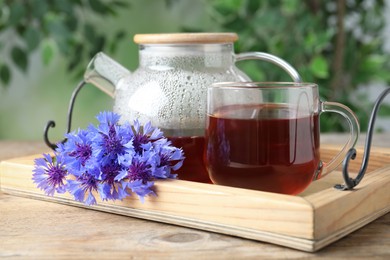 Photo of Tea set with hot drink and cornflowers on wooden table