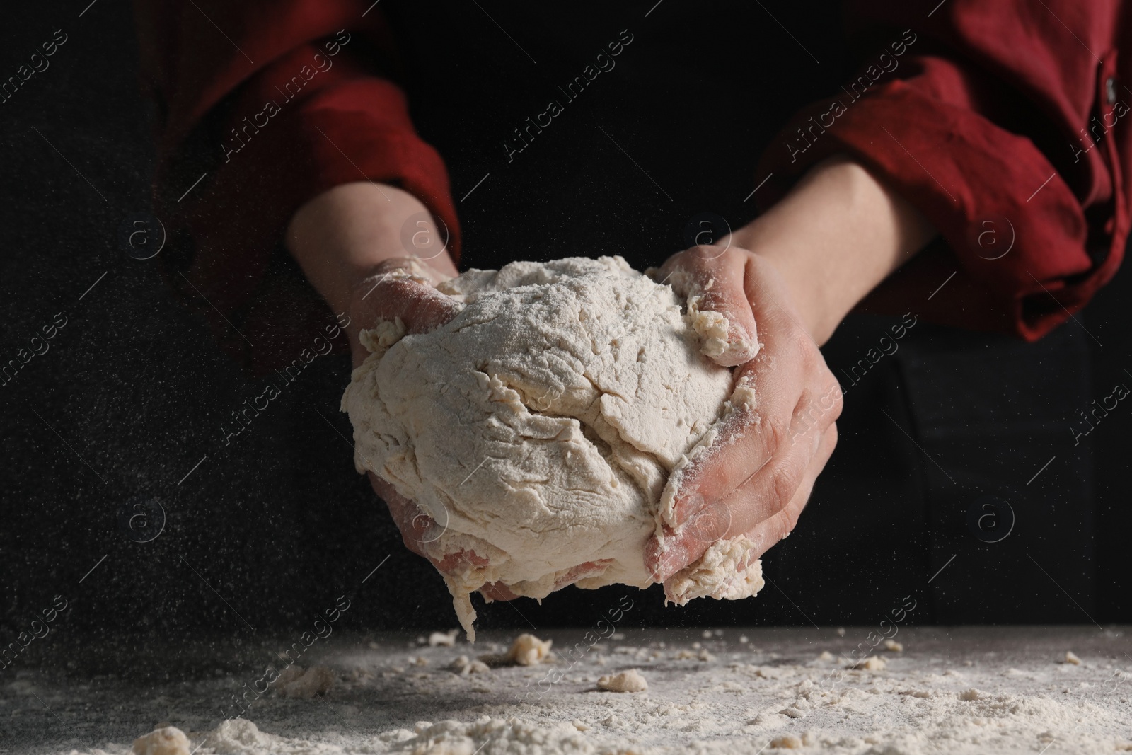 Photo of Making bread. Woman holding dough over table on dark background, closeup